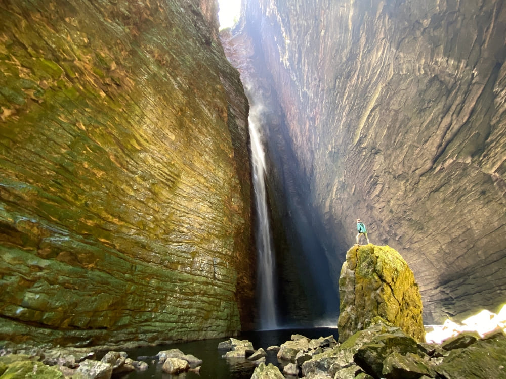 Person standing on a large rock admiring a gigantic waterfall cascading down immense rock walls in Chapada Diamantina.