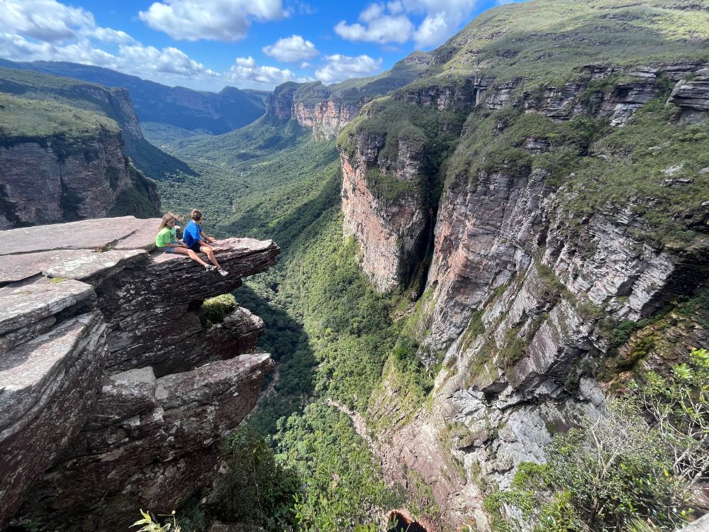 Two people sitting on the edge of a dramatic 300-meter-high canyon cliff at Cachoeirão, admiring the steep rocky walls. Two people sitting on the edge of a dramatic 300-meter-high canyon cliff at Cachoeirão, admiring the steep rocky walls.