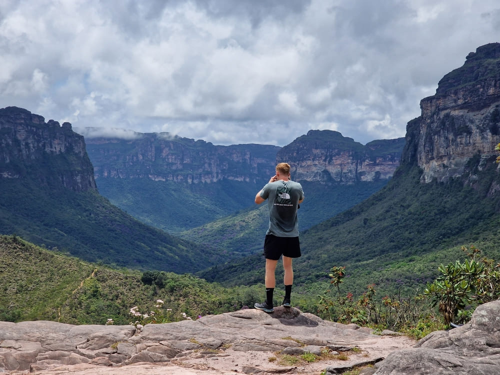 A hiker standing on a rocky outcrop taking a photograph of the sprawling green valleys and flat-topped mountains. A hiker standing on a rocky outcrop taking a photograph of the sprawling green valleys and flat-topped mountains.