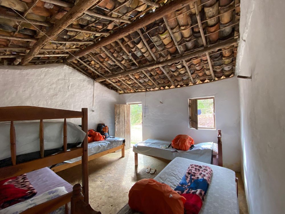 A shared homestay bedroom featuring wooden beds with sleeping bags and a rustic exposed tile and wood ceiling. A shared homestay bedroom featuring wooden beds with sleeping bags and a rustic exposed tile and wood ceiling.