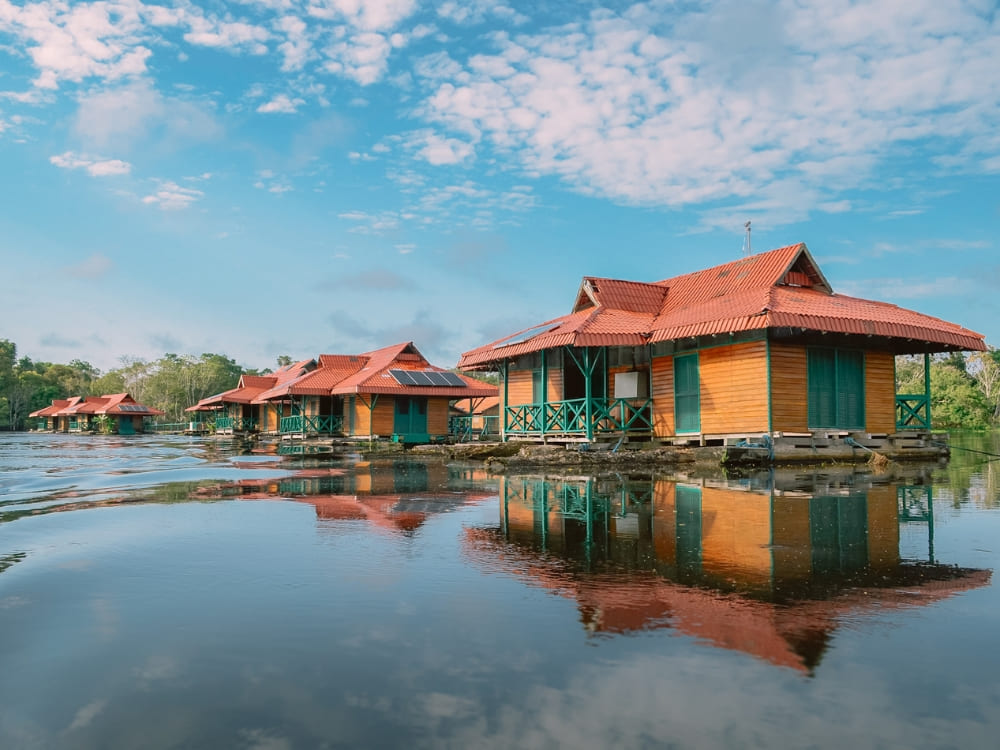Sustainable wooden Amazon jungle lodge cabins floating on a calm river reflecting the blue sky. Sustainable wooden Amazon jungle lodge cabins floating on a calm river reflecting the blue sky.