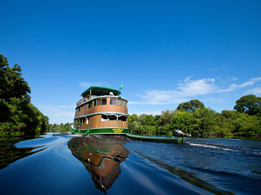 A multi-level traditional wooden river cruise boat navigates the reflective dark waters of the Amazon. A multi-level traditional wooden river cruise boat navigates the reflective dark waters of the Amazon.