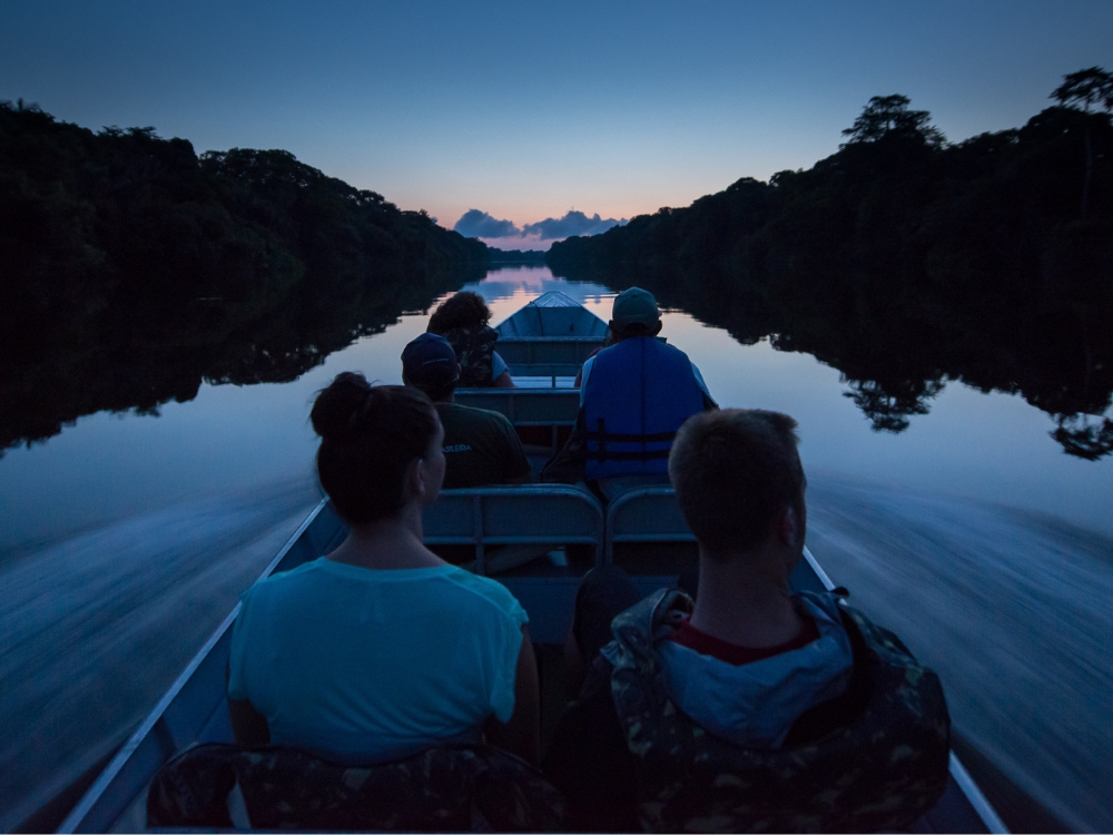 Tourists riding a motorized canoe exploring the calm waters of the Amazon Rainforest river at dusk Tourists riding a motorized canoe exploring the calm waters of the Amazon Rainforest river at dusk