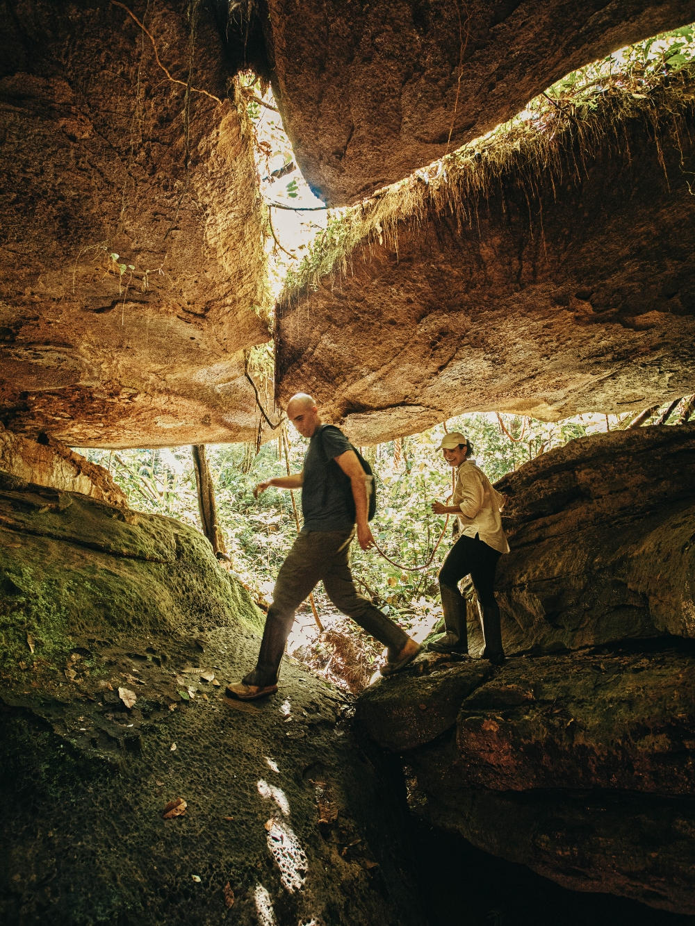 Two travelers hiking under a massive rock formation in the Presidente Figueiredo forest. Two travelers hiking under a massive rock formation in the Presidente Figueiredo forest.
