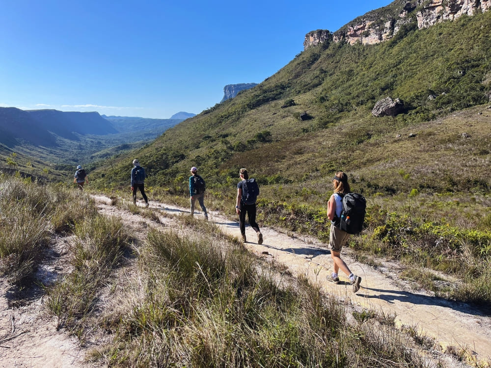 A group of hikers walks along a dirt trail surrounded by green mountains during the dry season in Chapada Diamantina National Park. A group of hikers walks along a dirt trail surrounded by green mountains during the dry season in Chapada Diamantina National Park.
