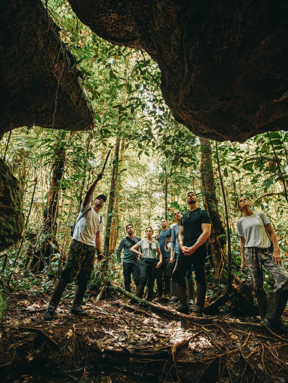 Group of tourists exploring a cave formation within the Amazon rainforest, looking out at the jungle with an expert local guide. Group of tourists exploring a cave formation within the Amazon rainforest, looking out at the jungle with an expert local guide.