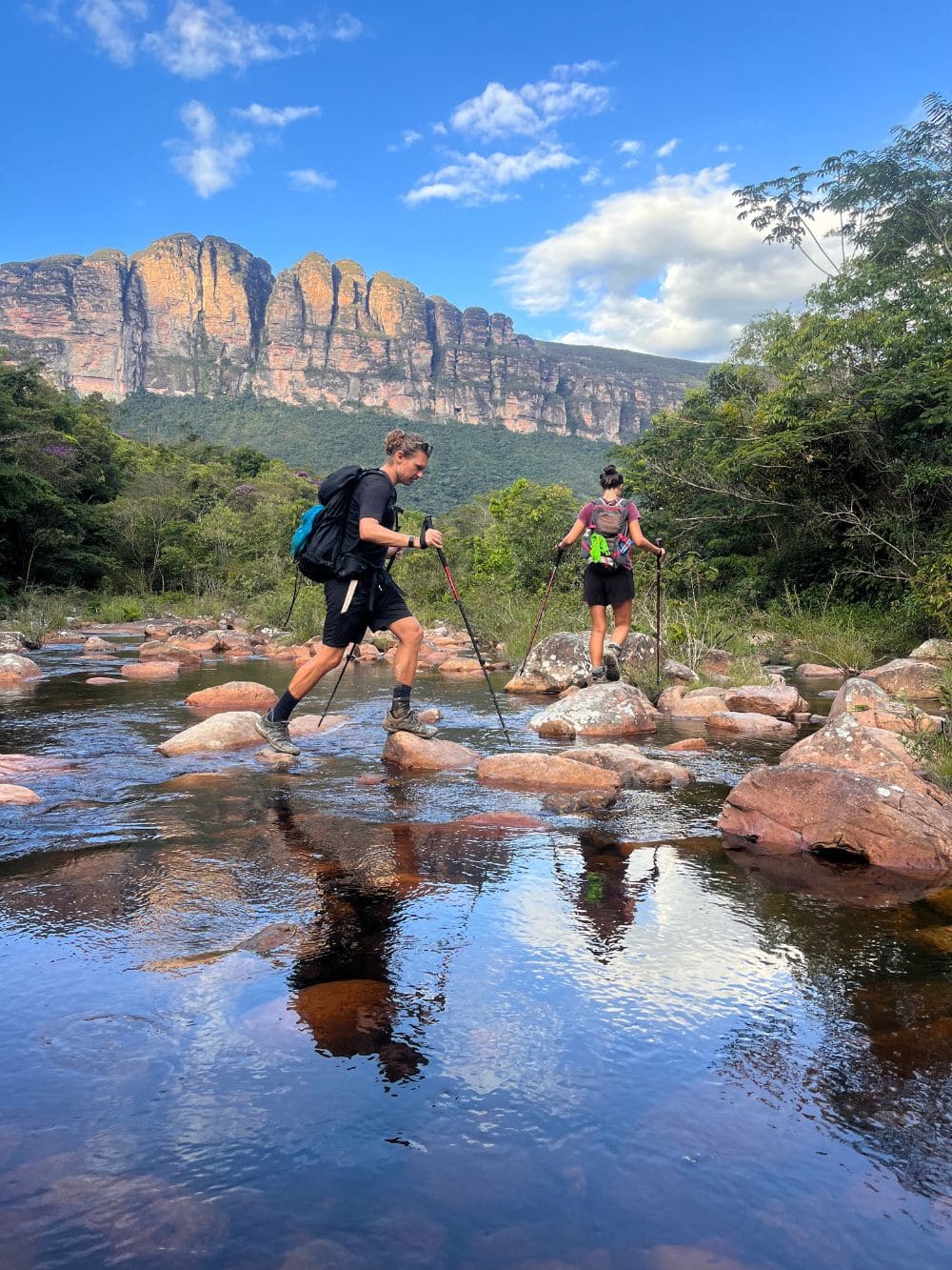Two hikers crossing a river using trekking poles during the Vale do Pati trek. 