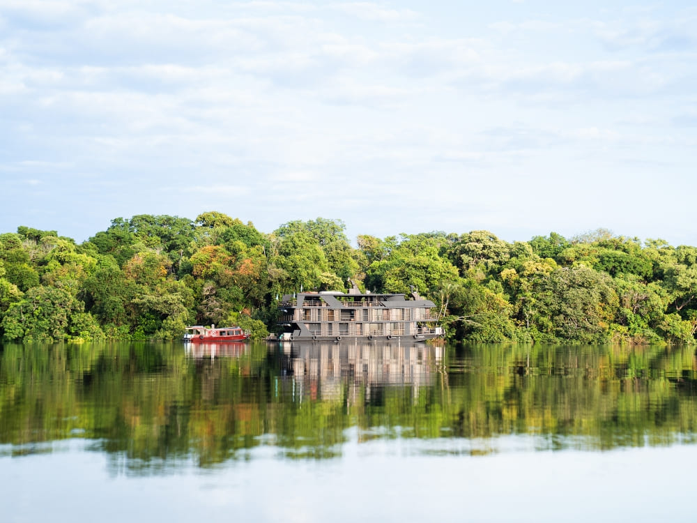 A multi-deck Amazon river cruise boat floating on calm waters reflecting the dense green forest vegetation. A multi-deck Amazon river cruise boat floating on calm waters reflecting the dense green forest vegetation.