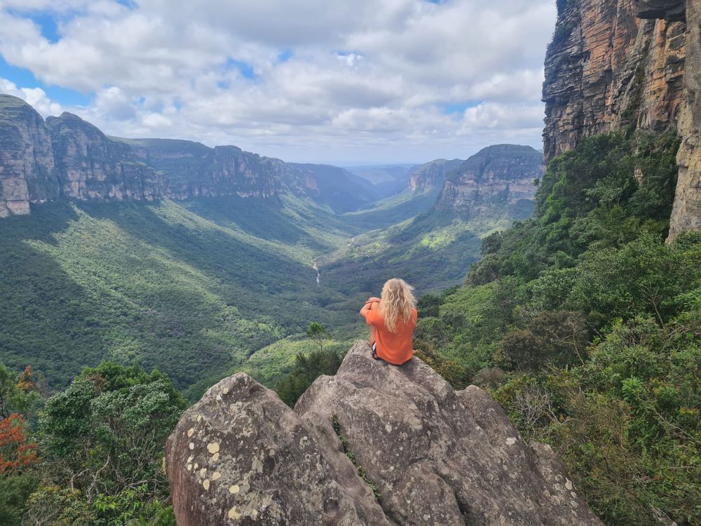 Tourist in an orange shirt sitting on a rock formation overlooking the vastness of a green valley in Chapada Diamantina. Tourist in an orange shirt sitting on a rock formation overlooking the vastness of a green valley in Chapada Diamantina.