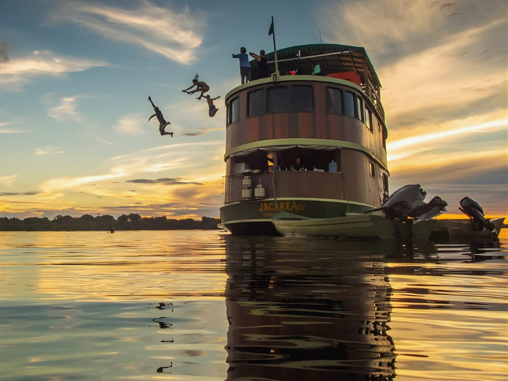 Travelers jumping from the top deck of a river cruise boat into the Amazon River at sunset during an adventurous ecotourism trip Travelers jumping from the top deck of a river cruise boat into the Amazon River at sunset during an adventurous ecotourism trip