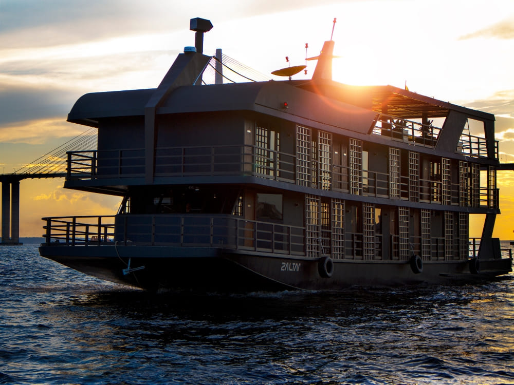 The Zaltana luxury riverboat anchored in the Amazon river at sunset, showing its modern design and spacious structure for a premium cruise. The Zaltana luxury riverboat anchored in the Amazon river at sunset, showing its modern design and spacious structure for a premium cruise.