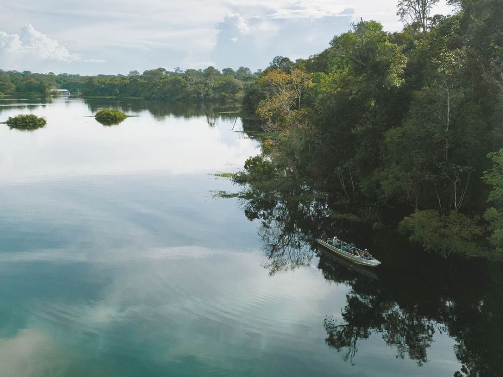 Small boat navigating in the distance on the calm and reflective waters of the Mamori River, surrounded by green jungle vegetation.