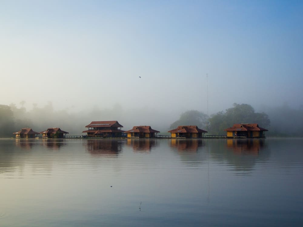 Uakari Lodge floating inn made of wooden cabins on the calm waters of Lake Mamirauá with mist in the background.