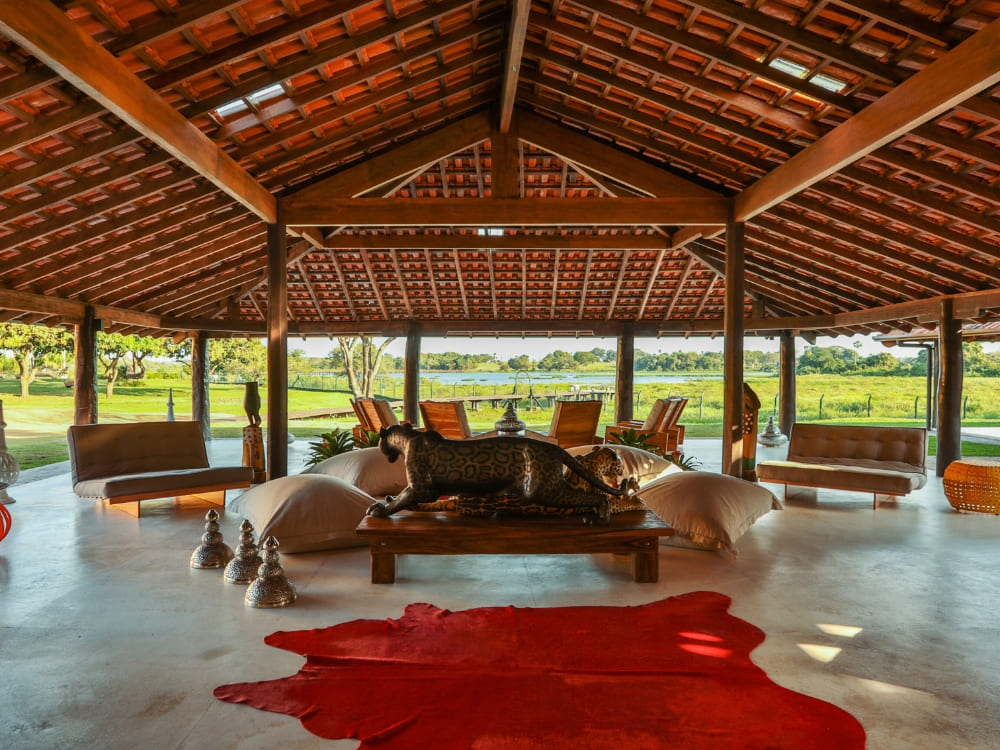Open-air living room featuring a red cowhide rug and a carved wooden jaguar at Caiman ecolodge. Open-air living room featuring a red cowhide rug and a carved wooden jaguar at Caiman ecolodge.