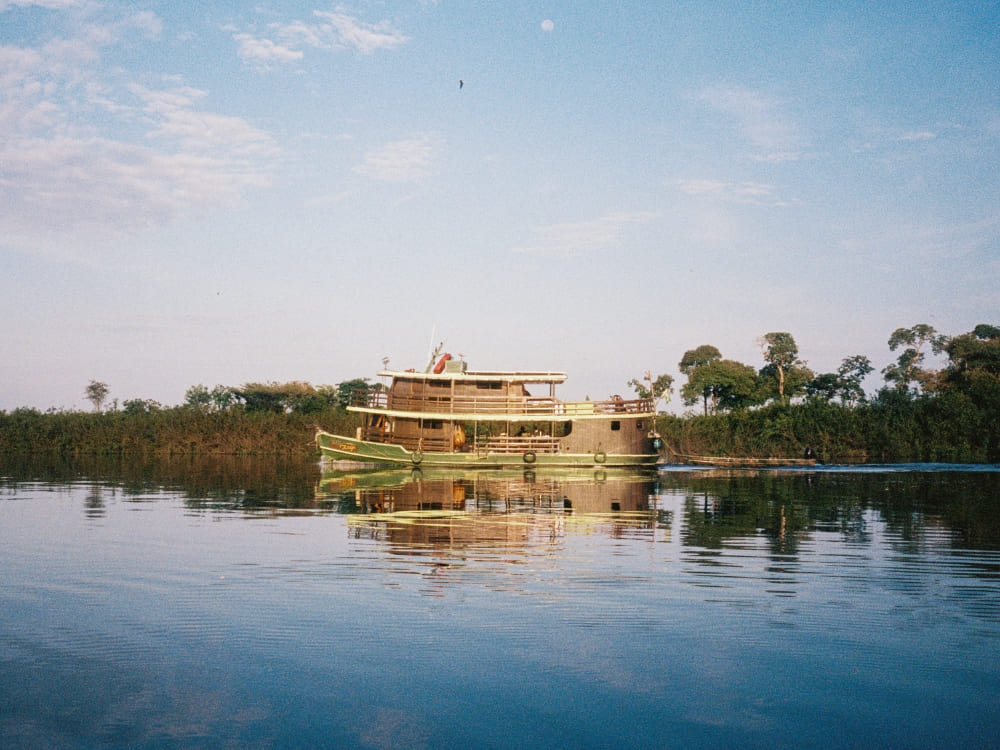 Traditional river cruise boat navigating the calm waters of the Rio Negro, with green vegetation reflecting on the water. Traditional river cruise boat navigating the calm waters of the Rio Negro, with green vegetation reflecting on the water.