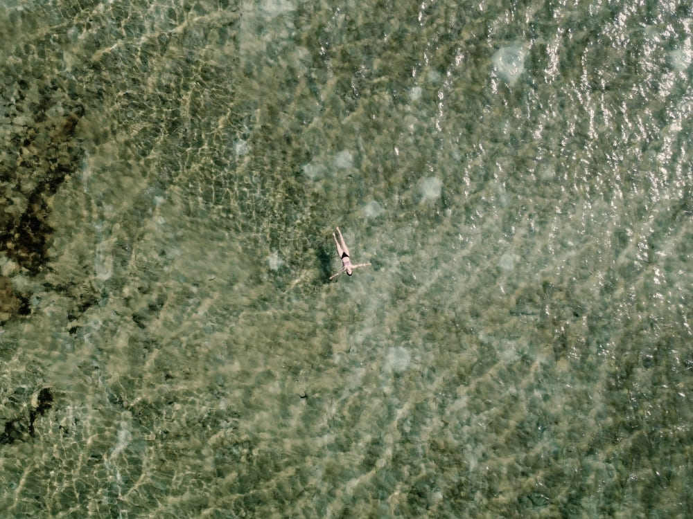  Top-down view of a person swimming in crystal-clear, shallow water over a textured sandy bottom during a Lençóis Maranhenses tour. 