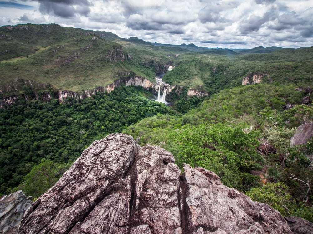 View from a rocky overlook showing a distant waterfall and lush vegetation in Chapada dos Veadeiros National Park. View from a rocky overlook showing a distant waterfall and lush vegetation in Chapada dos Veadeiros National Park.