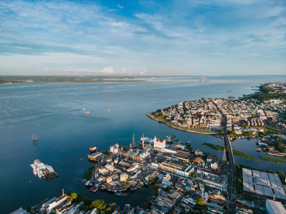 Aerial view of Manaus, Amazonas, showing the city's port, residential neighborhoods, and the expansive river with a long bridge in the distance. Aerial view of Manaus, Amazonas, showing the city's port, residential neighborhoods, and the expansive river with a long bridge in the distance.