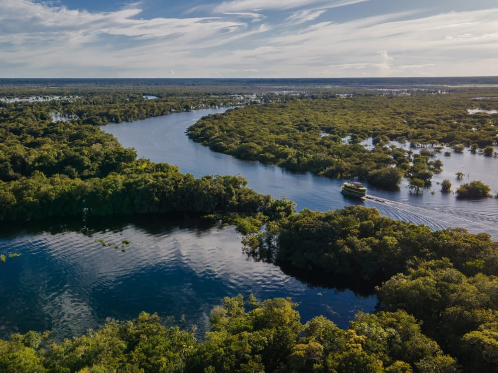 A riverboat cruising through the winding waters of the Amazon River surrounded by lush rainforest. A riverboat cruising through the winding waters of the Amazon River surrounded by lush rainforest.