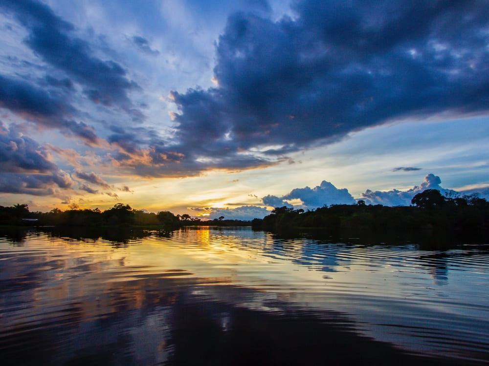 A colorful sunset reflecting on the calm waters of the Amazon River bordered by the rainforest. A colorful sunset reflecting on the calm waters of the Amazon River bordered by the rainforest.
