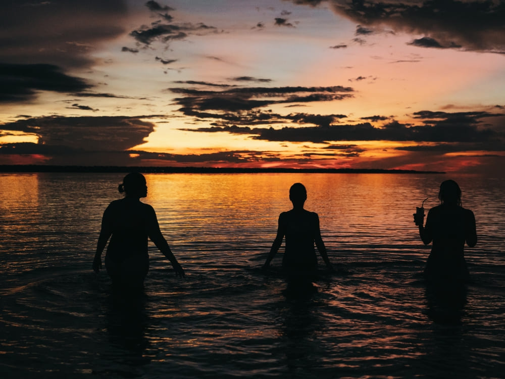 Silhouettes of three people standing waist-deep in the waters of the Amazon at sunset. Silhouettes of three people standing waist-deep in the waters of the Amazon at sunset.