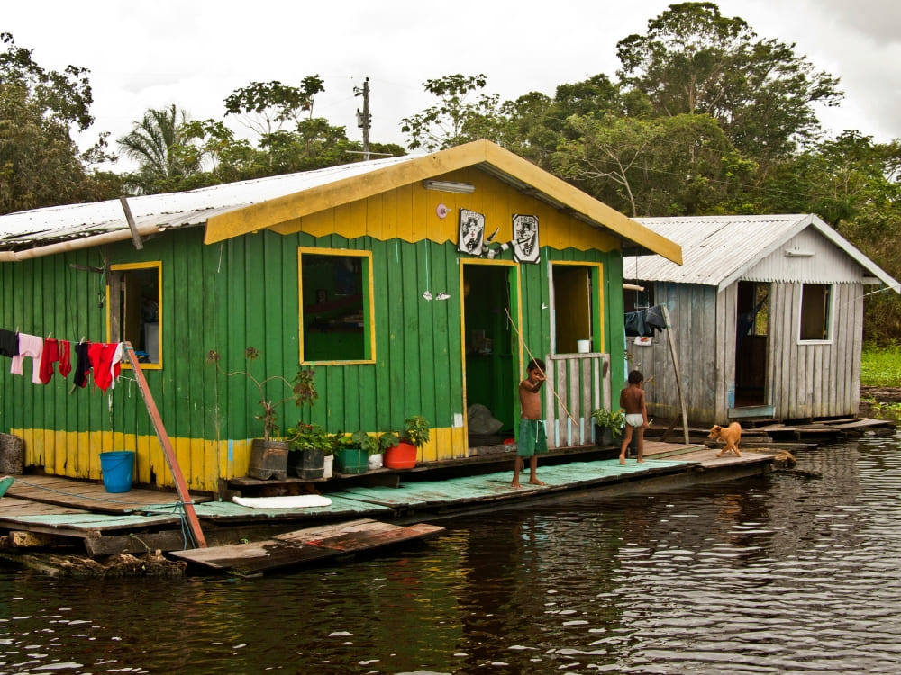 Children standing outside a vibrant green and yellow floating house on the waters of the Amazon River. Children standing outside a vibrant green and yellow floating house on the waters of the Amazon River.