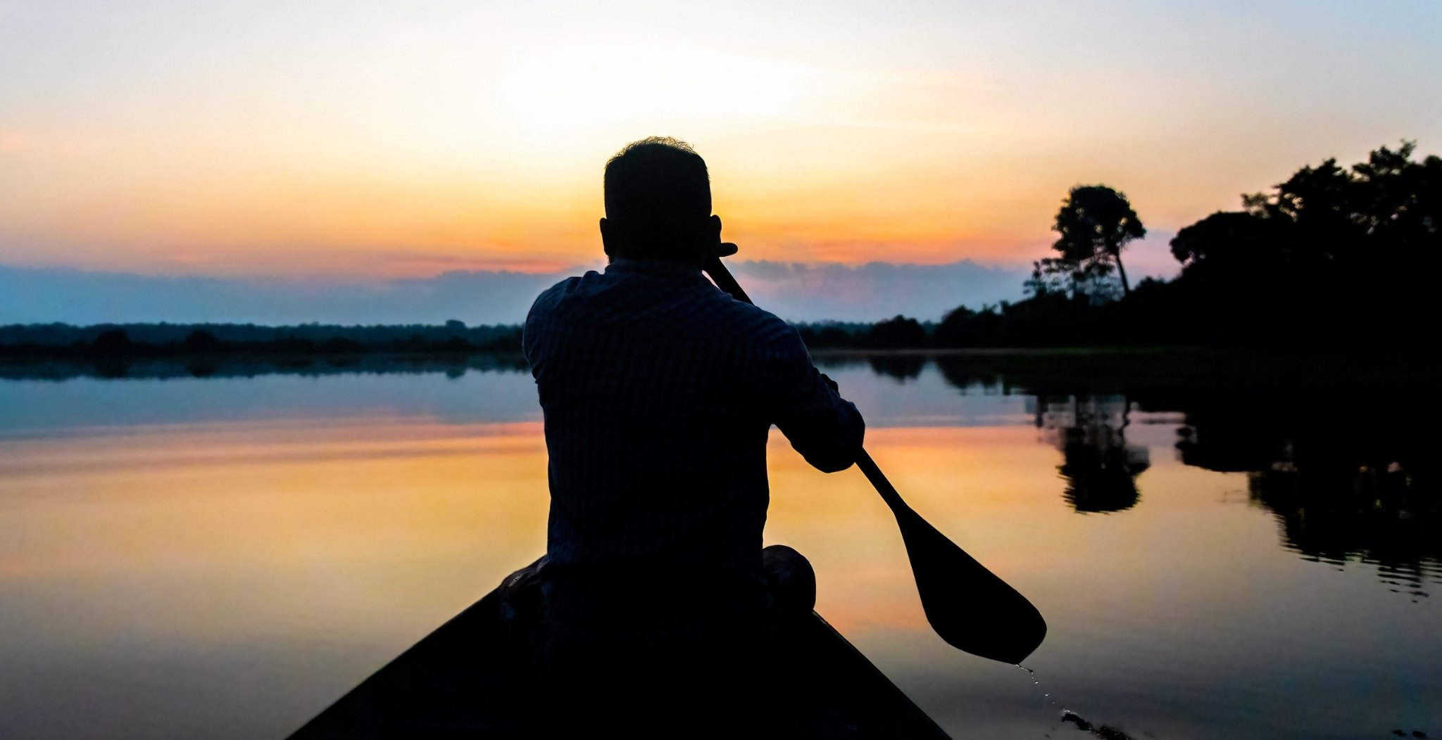 Traveler canoeing at sunset on a calm lake during an Amazon boutique lodge stay in Brazil