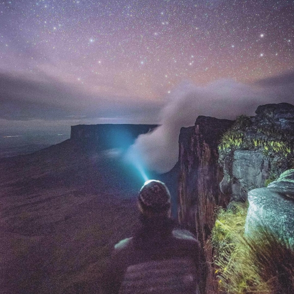 Um céu estrelado sobre o Monte Roraima com a lanterna de cabeça de um trekker acesa