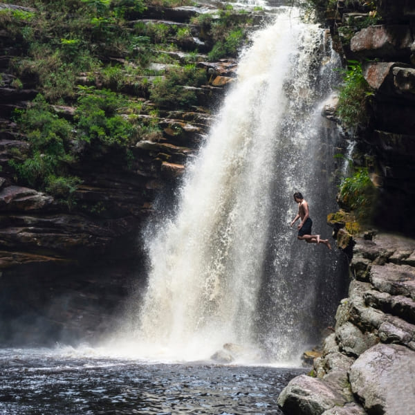 Banhista pulando no poço natural sob uma cachoeira na Chapada Diamantina, Brasil.