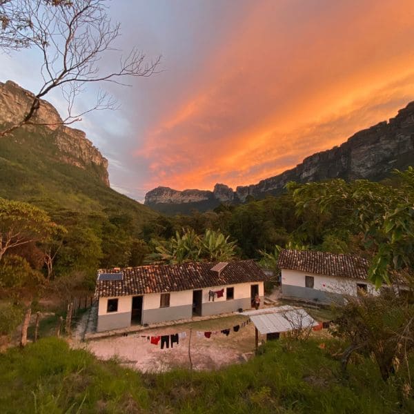 Casas de nativos no Vale do Pati sob um céu alaranjado ao pôr do sol, na Chapada Diamantina, Brasil.