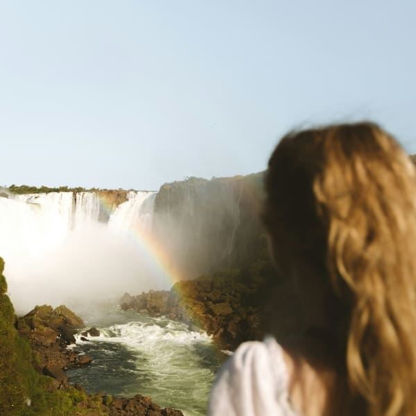 Visitante observando as Cataratas do Iguaçu com um arco-íris na neblina de água, Brasil.