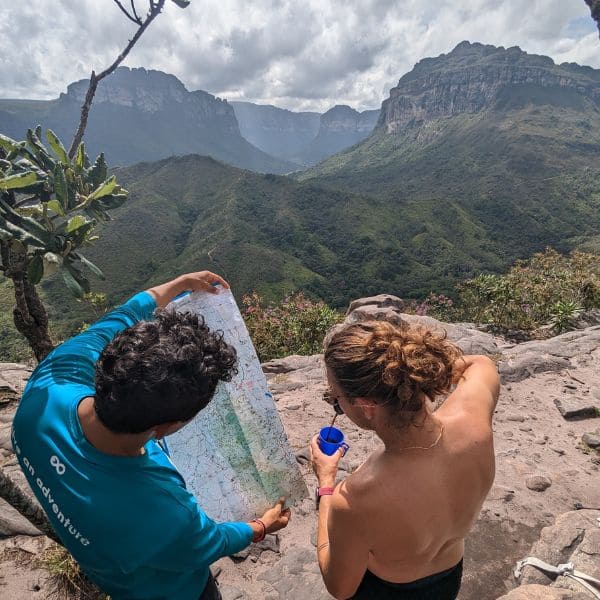 Dois trilheiros olhando o mapa da trilha sobre uma pedra, acima dos cânions do Vale do Pati, na Chapada Diamantina, Brasil.