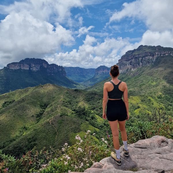 Trilheira sobre uma pedra observando o vale verde e os morros de topo plano do Vale do Pati, na Chapada Diamantina, Brasil.