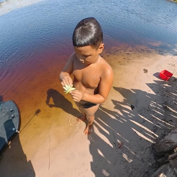 Un niño del lugar sostiene una flor a orillas de una laguna
