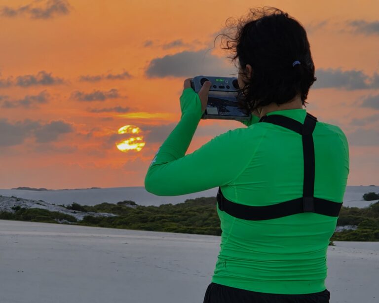 Producer Jihee Yeon filming the Lençóis Maranhenses dunes under an orange sky with a drone controller Producer Jihee Yeon filming the Lençóis Maranhenses dunes under an orange sky with a drone controller